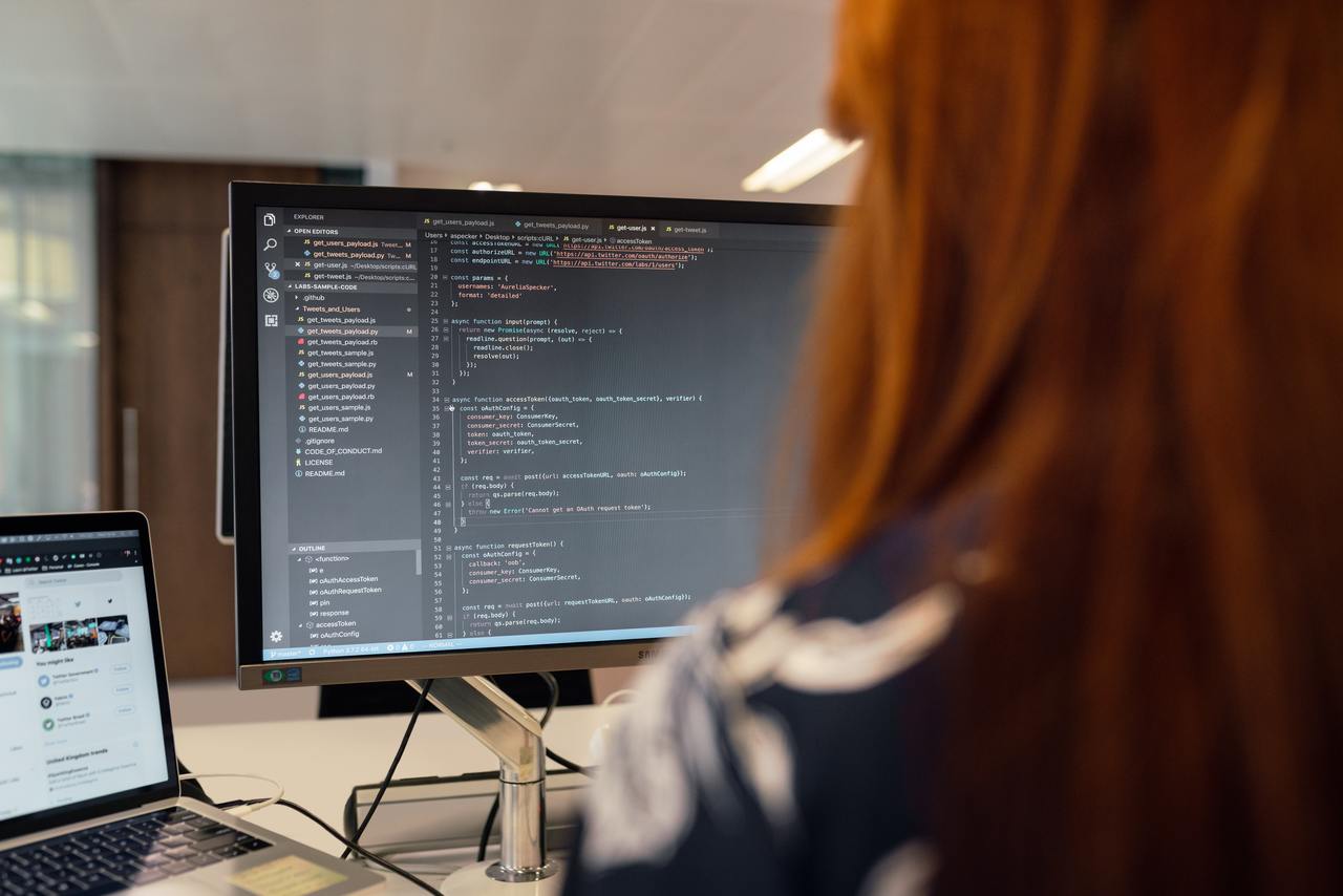 Рыжеволосая женщина работает в сфере разработки программ:  пишет код.